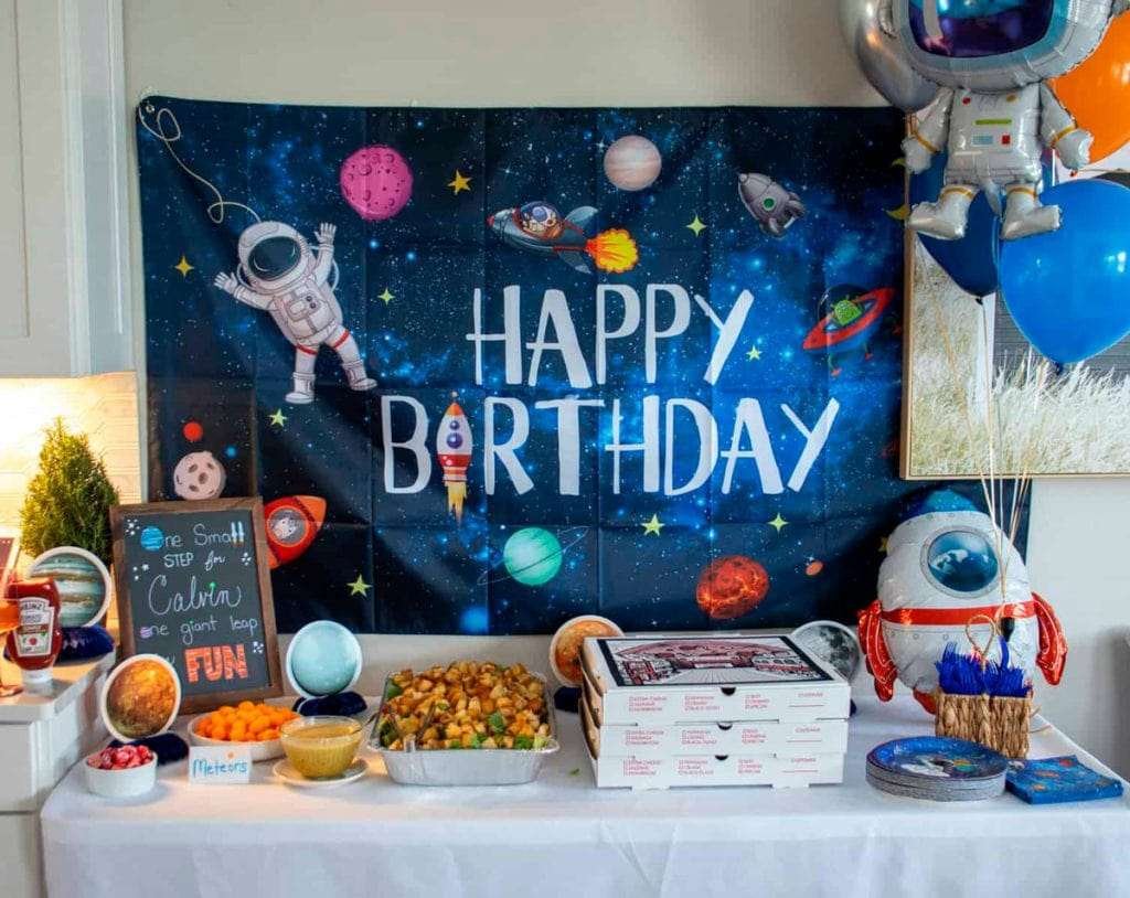 Best First and Second Birthday Party Ideas for Boys and Girls 158 Outer space themed birthday party with astronaut balloons, planets, stars and rocket decorations in a horizontal layout.
