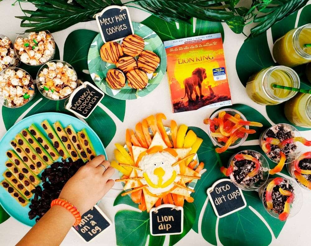 Best First and Second Birthday Party Ideas for Boys and Girls 62 Safari party snack table with fruit skewers, lion dip and snacks labeled “Lion Bites”, “Elephant Treats,” and “Tiger Tails.”